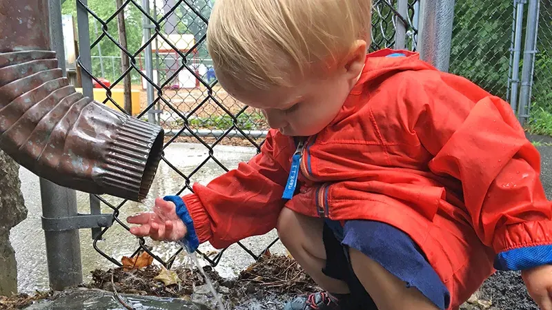 Young boy playing in water from downspout